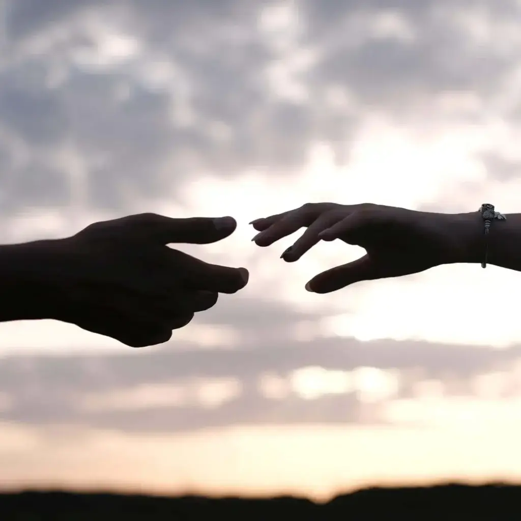 Silhouettes of two hands reaching for each other, backlit by a rising sun.