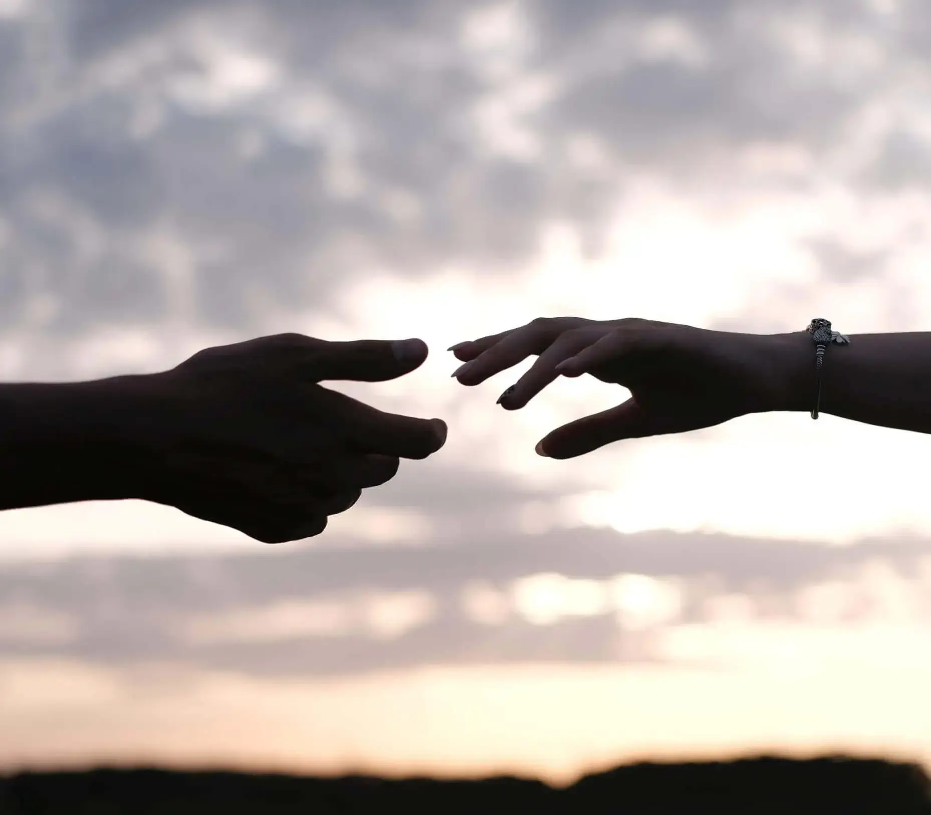 Silhouettes of two hands reaching for each other, backlit by a rising sun.
