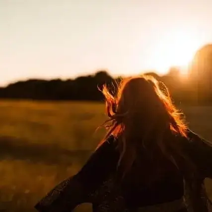 Back view of a woman running freely through a field.