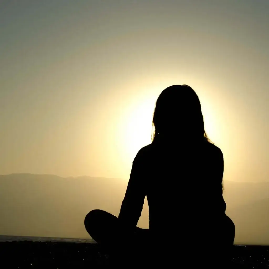 The silhouette of a person meditating against a background of a rising sun.